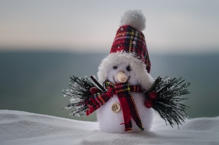 New Year Christmas concept. The snowman stands on snow with blurred nature background. White snowman surrounded by Christmas trees on evening background. Toy Decoration. Selective focus. Empty spaceの写真素材