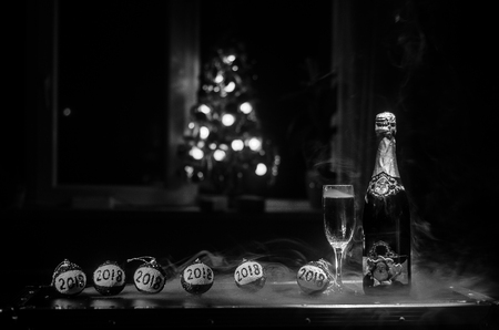 New Year Eve celebration background with pair of flutes and bottle of champagne with Christmas attributes (or elements) on snowy dark toned foggy background. Selective focus. Useful as greeting cardの写真素材
