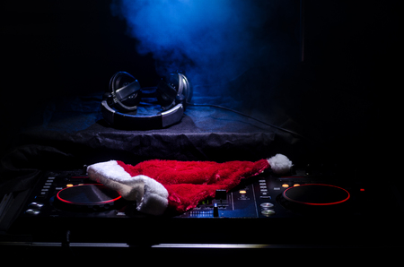 Dj mixer with headphones on dark nightclub background with Christmas tree New Year Eve. Close up view of New Year elements or symbols (Santa Clause, Snowman, Dog 2018, gift box) on a Dj table.の写真素材