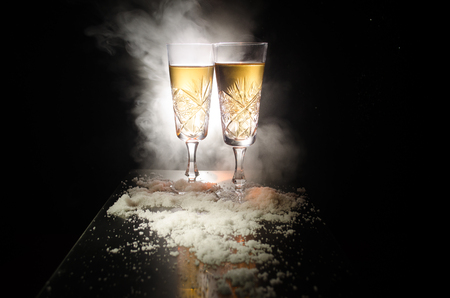 New Year Eve celebration background with pair of flutes and bottle of champagne with Christmas attributes (or elements) on snowy dark toned foggy background. Selective focus. Useful as greeting cardの写真素材