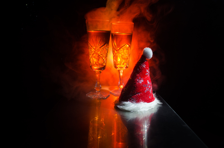 New Year Eve celebration background with pair of flutes and bottle of champagne with Christmas attributes (or elements) on snowy dark toned foggy background. Selective focus. Useful as greeting cardの写真素材