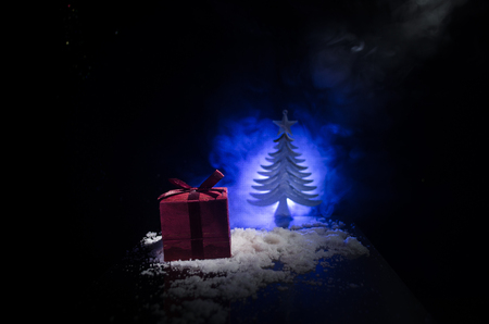 Red Christmas gift box and fir tree on snow. Christmas home decoration with snow and tree on a dark background with copy space. Selective focus. New Year attributes on backgroundの写真素材