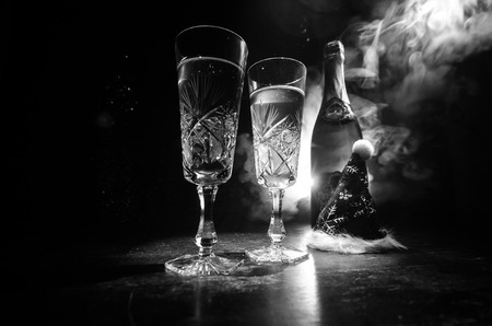 New Year Eve celebration background with pair of flutes and bottle of champagne with Christmas attributes (or elements) on snowy dark toned foggy background. Selective focus. Useful as greeting cardの写真素材