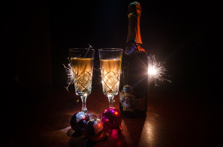 New Year Eve celebration background with pair of flutes and bottle of champagne with Christmas attributes (or elements) on snowy dark toned foggy background. Selective focus. Useful as greeting cardの写真素材