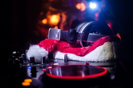 Dj mixer with headphones on dark nightclub background with Christmas tree New Year Eve. Close up view of New Year elements or symbols (Santa Clause, Snowman, Dog 2018, gift box) on a Dj table.の写真素材