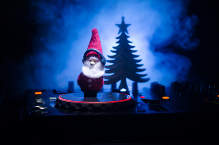 Dj mixer with headphones on dark nightclub background with Christmas tree New Year Eve. Close up view of New Year elements or symbols (Santa Clause, Snowman, Dog 2018, gift box) on a Dj table.の写真素材