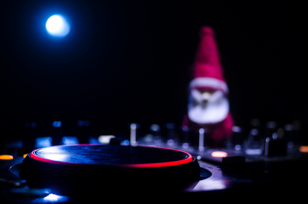 Dj mixer with headphones on dark nightclub background with Christmas tree New Year Eve. Close up view of New Year elements or symbols (Santa Clause, Snowman, Dog 2018, gift box) on a Dj table.の写真素材