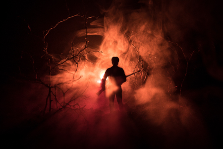 Man with riffle at spooky forest at night with lightの写真素材