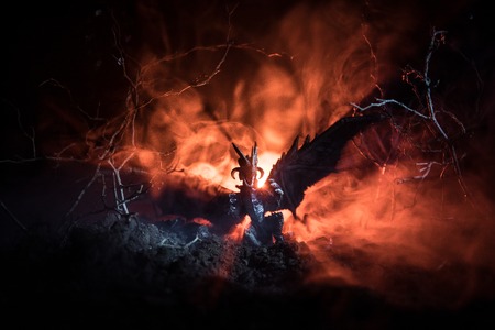 Silhouette of fire breathing dragon with big wings on a dark orange backgroundの写真素材