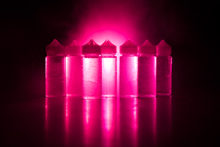 Vape concept. Smoke clouds and vape liquid bottles on dark background. Light effects. Selective...