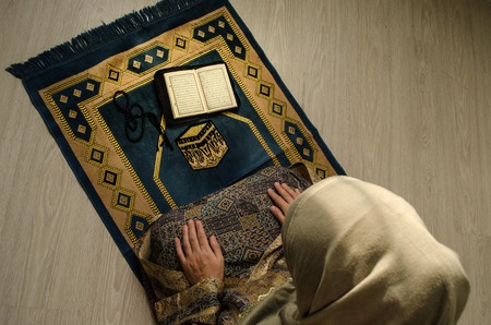 Muslim woman praying for Allah muslim god at room near window. Hands of muslim woman on the carpet praying in traditional wearing clothes, Woman in Hijab, Carpet of Kaaba, Selective focus, tonedの写真素材