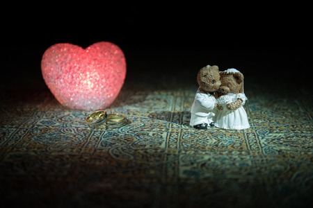 Stuffed bride and groom bears standing together with LED heart on dark foggy background. Selective focusの写真素材