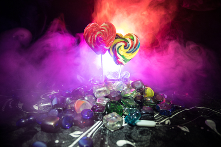 Few colorful candy heart lollipops on different colored candies against dark toned foggy background. Selective focusの写真素材