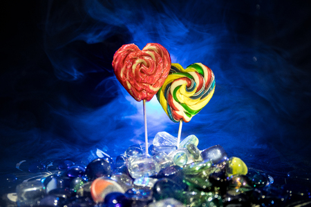 Few colorful candy heart lollipops on different colored candies against dark toned foggy background. Selective focusの写真素材