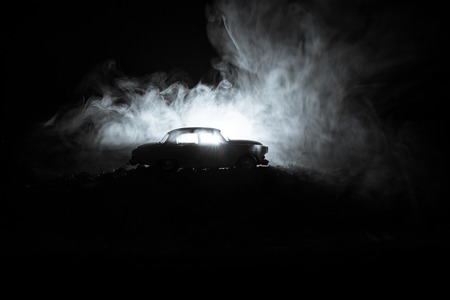 Silhouette of old vintage car in dark foggy toned background with glowing lights in low light, or silhouette of old crime car dark background. Selective focusの写真素材