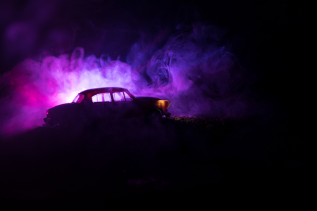 Silhouette of old vintage car in dark foggy toned background with glowing lights in low light, or silhouette of old crime car dark background. Selective focusの写真素材