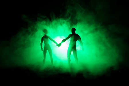 Love Valentine`s Day concept.Sillhouette of sweet young couple in love standing in the field and hugging on dark toned foggy background. Decoration with doll figures on table shot. Selective focusの写真素材
