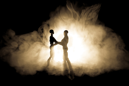 Love Valentine`s Day concept.Sillhouette of sweet young couple in love standing in the field and hugging on dark toned foggy background. Decoration with doll figures on table shot. Selective focusの写真素材