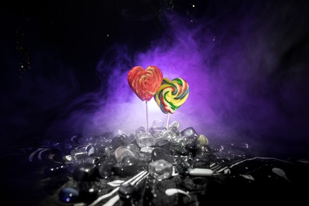 Few colorful candy heart lollipops on different colored candies against dark toned foggy background. Selective focusの写真素材