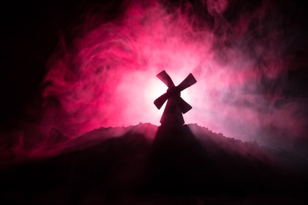 Windmill silhouette standing on hill against the night sky. Night decor with old windmill on hill with horror toned foggy background with light. Horror conceptの写真素材