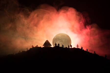 Scary view crowd of zombies on hill with spooky cloudy sky with fog and rising full moon. Silhouette group of zombie walking under full moon. Halloween concept.の写真素材