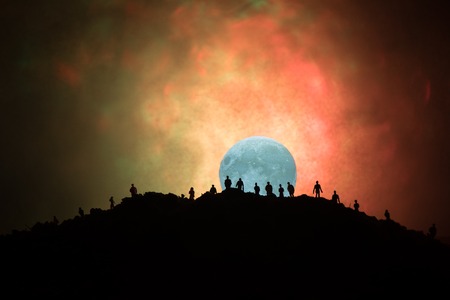 Scary view crowd of zombies on hill with spooky cloudy sky with fog and rising full moon. Silhouette group of zombie walking under full moon. Halloween concept.の写真素材