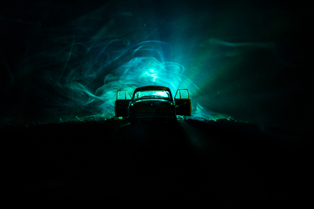 Silhouette of old vintage car in dark foggy toned background with glowing lights in low lightSelective focusの写真素材