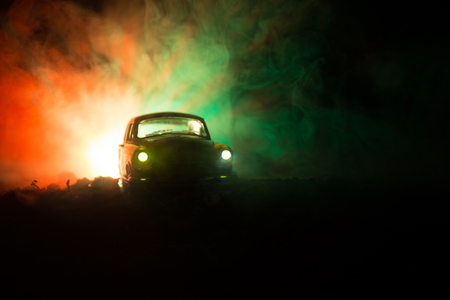 Silhouette of old vintage car in dark foggy toned background with glowing lights in low lightの写真素材
