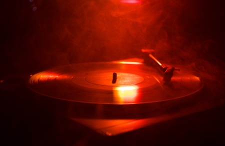Turntable vinyl record player. Retro audio equipment for disc jockey. Sound technology for DJ to mix & play music. Vinyl record being played against burning fire background with smokeの写真素材
