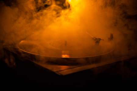 Turntable vinyl record player. Retro audio equipment for disc jockey. Sound technology for DJ to mix & play music. Vinyl record being played against burning fire background with smokeの写真素材