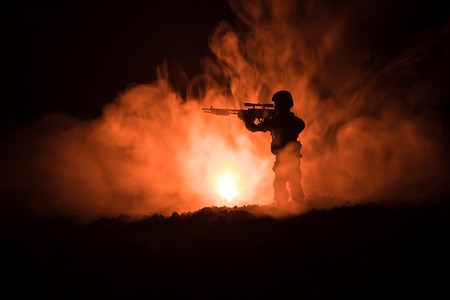 Silhouette of military sniper with sniper gun at dark toned foggy background. shot, holding gun, colorful sky, background. Selective focusの写真素材