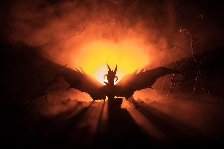Silhouette of fire breathing dragon with big wings on a dark orange backgroundの写真素材