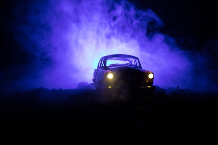 Silhouette of old vintage car in dark foggy toned background with glowing lights in low light, or silhouette of old crime car dark background. Selective focusの写真素材