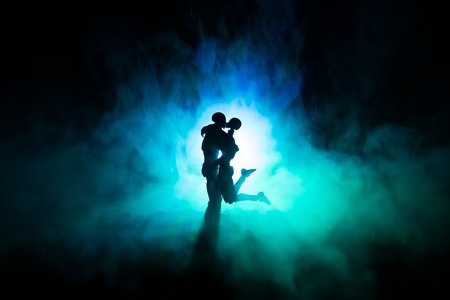 Love Valentine`s Day concept.Sillhouette of sweet young couple in love standing in the field and hugging on dark toned foggy background. Decoration with doll figures on table shot. Selective focusの写真素材