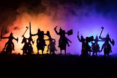 Medieval battle scene with cavalry and infantry. Silhouettes of figures as separate objects, fight between warriors on dark toned foggy background. Night scene. Selective focusの写真素材