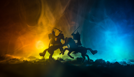 Medieval battle scene with cavalry and infantry. Silhouettes of figures as separate objects, fight between warriors on dark toned foggy background. Night scene. Selective focusの写真素材
