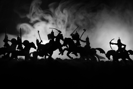 Medieval battle scene with cavalry and infantry. Silhouettes of figures as separate objects, fight between warriors on dark toned foggy background. Night scene. Selective focusの写真素材