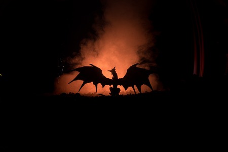 Silhouette of fire breathing dragon with big wings on a dark orange background. Selective focusの写真素材