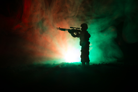 Silhouette of military sniper with sniper gun at dark toned foggy background. shot, holding gun, colorful sky, background. Selective focusの写真素材