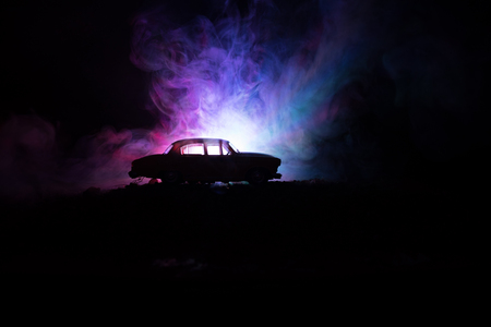 Silhouette of old vintage car in dark foggy toned background with glowing lights in low light, or silhouette of old crime car dark background. Selective focusの写真素材