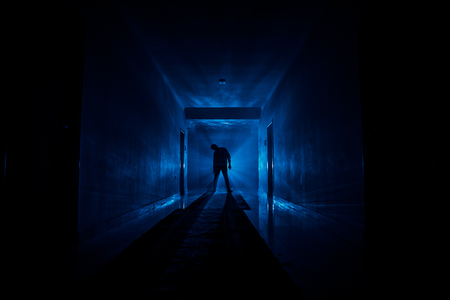 Creepy silhouette in the dark abandoned building. Horror about maniac concept or Dark corridor with cabinet doors and lights with silhouette of spooky horror person standing with different poses.の素材 [FY31097102259]