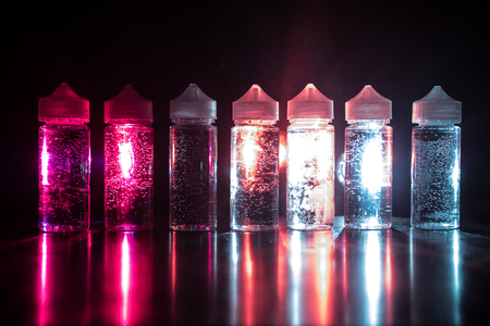 Vape concept. Smoke clouds and vape liquid bottles on dark background. Light effects. Selective focusの写真素材