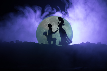 Amazing love scene. Silhouettes of man making proposal to woman or Silhouettes of couple against big moon at background. Selective focusの写真素材