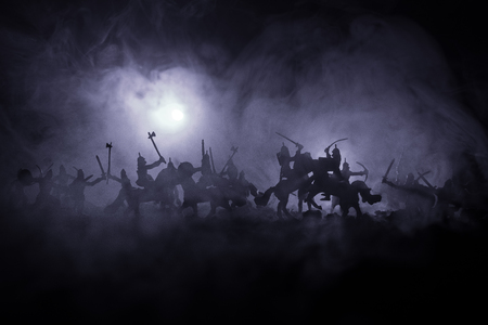 Medieval battle scene with cavalry and infantry. Silhouettes of figures as separate objects, fight between warriors on dark toned foggy background. Night scene. Selective focusの写真素材
