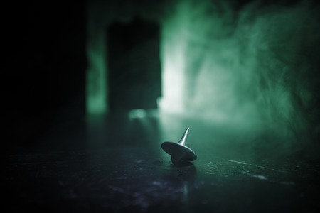 Totem spinning top spinning, wobbling and stopping. Spinning top on mirror surface with toned smoke background light. Whirligig in action in dark room on table. Selective focusの写真素材