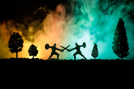 Medieval battle scene with cavalry and infantry. Silhouettes of figures as separate objects, fight between warriors on dark toned foggy background. Night scene. Selective focusの写真素材