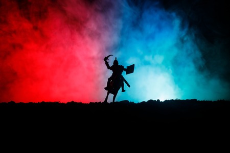 Medieval battle scene with cavalry and infantry. Silhouettes of figures as separate objects, fight between warriors on dark toned foggy background. Night scene. Selective focusの写真素材