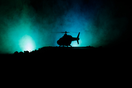 Silhouette of military helicopter ready to fly from conflict zone. Decorated night footage with helicopter starting in desert with foggy toned backlit. Selective focus. War conceptの写真素材