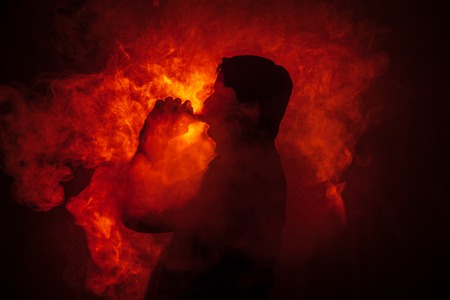 Vaping man holding a mod. A cloud of vapor. dark foggy toned background of clouds of smoke. Vaping an electronic cigarette with a lot of smoke. Vape concept. Selective focusの写真素材