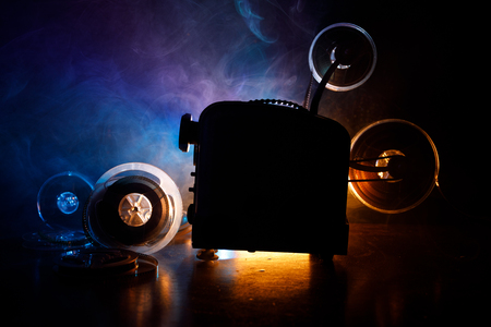 Old style movie projector, still-life, close-up. Film projector on a wooden background with dramatic lighting and selective focus. Movies and entertainment conceptの写真素材